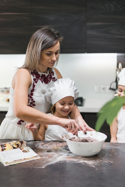 Madre e hijos preparando la masa en el mostrador de la cocina desordenada