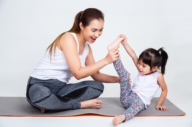 Madre enseñando a hija linda a estirar los músculos de las piernas.