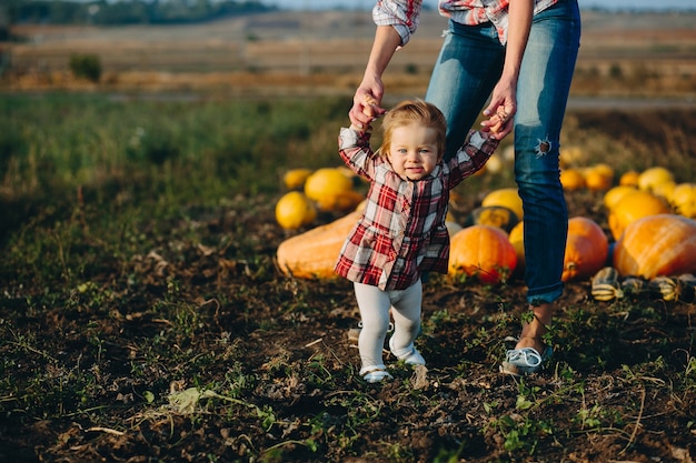 Madre enseñando a su hija a caminar por el campo con calabazas, víspera de Halloween