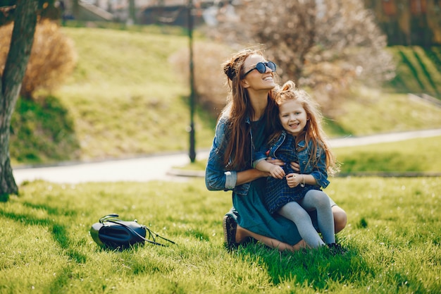 madre con estilo con el pelo largo y una chaqueta de jeans jugando con su pequeña hija linda