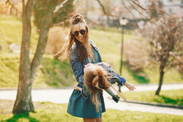 madre con estilo con el pelo largo y una chaqueta de jeans jugando con su pequeña hija linda