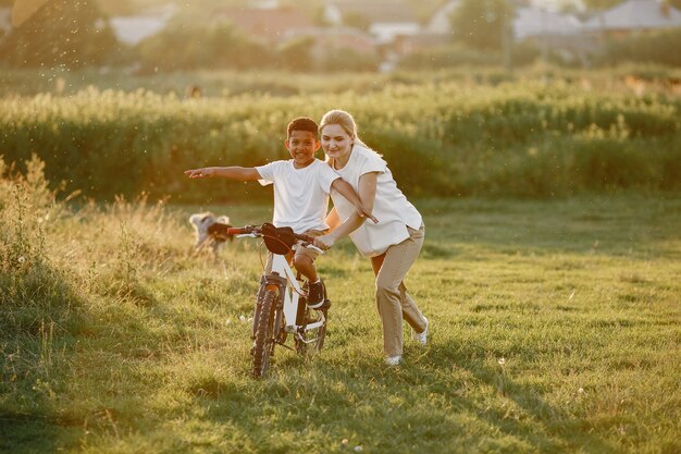 Madre europea e hijo africano. Familia en un parque de verano. Niño con bicicleta.