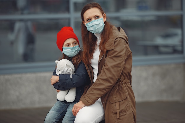 Foto gratuita una madre europea en un respirador con su hija está parada cerca de un edificio. el padre le está enseñando a su hijo cómo usar una máscara protectora para salvarse del virus.