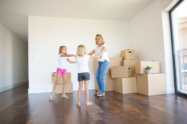 Madre feliz bailando con dos niñas entre cajas desempaquetadas