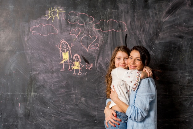 Madre feliz e hija que abrazan cerca de la pizarra con el dibujo