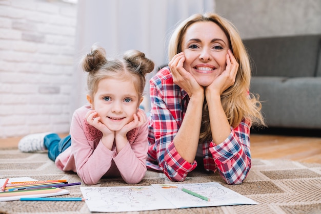 Madre feliz e hija que miran la cámara en sala de estar