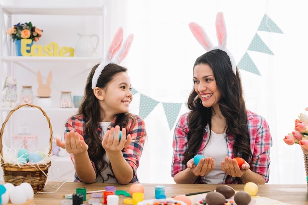 Madre feliz e hija que sostienen los huevos de Pascua a mano que se miran en casa