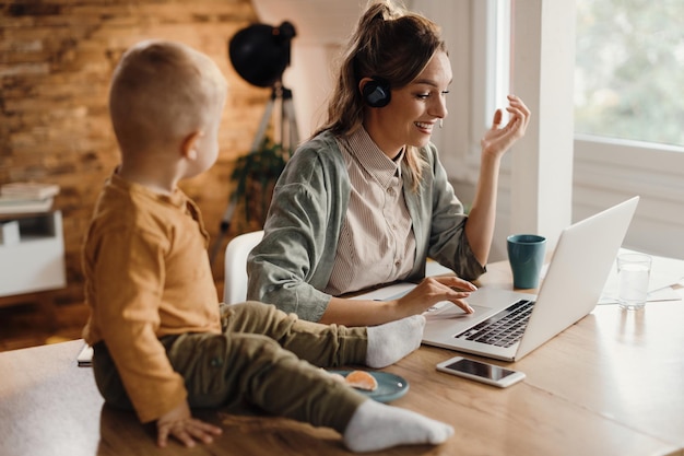 Foto gratuita madre feliz haciendo videollamadas a través de una computadora portátil mientras trabaja en casa