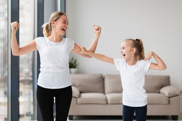 Madre feliz mostrando bíceps a hija sonriente