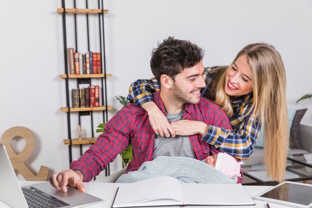 Madre feliz que abraza al padre con el bebé en el escritorio