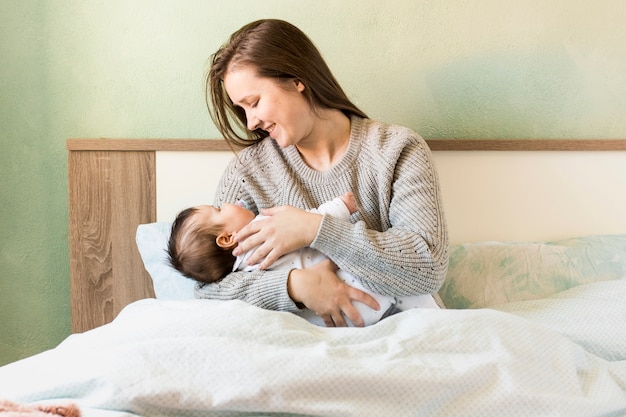 Madre feliz que celebra al bebé en brazos en cama