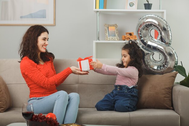 Madre feliz recibiendo presente de su pequeña hija. Celebrando el día internacional de la mujer el 8 de marzo