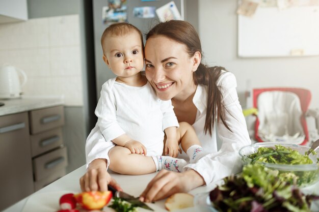 Madre feliz sonriente con su bebé posando en la cocina