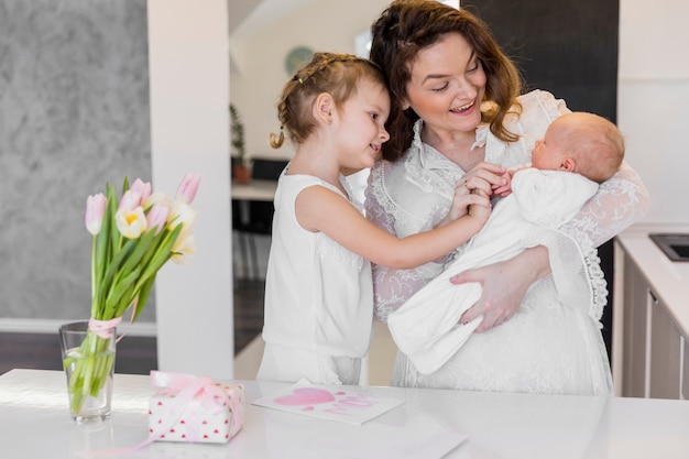 Madre feliz con sus dos lindos niños de pie junto a la mesa blanca