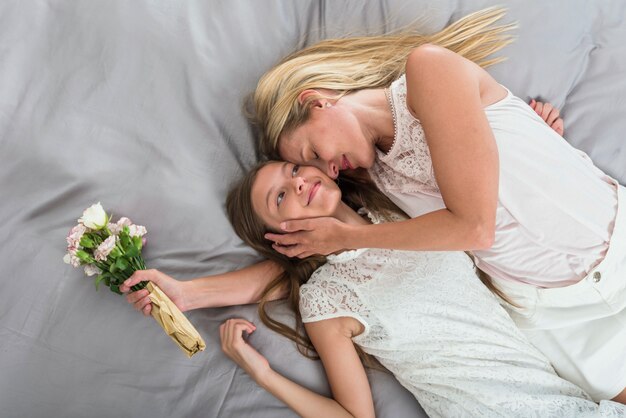 Madre con flores abrazando a hija en cama