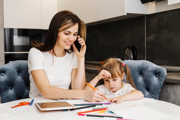 Foto gratuita madre hablando por teléfono y ayudando a su hija