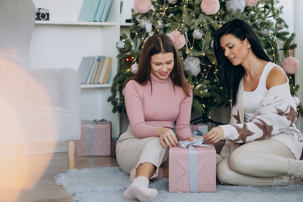 Madre con hija adulta con regalos de navidad por árbol de navidad