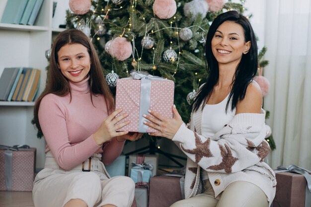 Madre con hija adulta con regalos de navidad por árbol de navidad