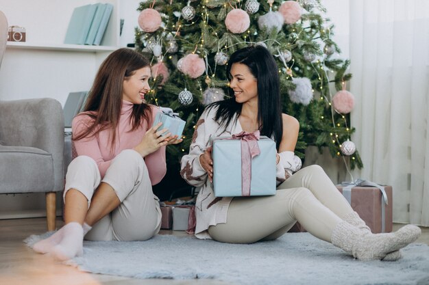 Madre con hija adulta con regalos de navidad por árbol de navidad