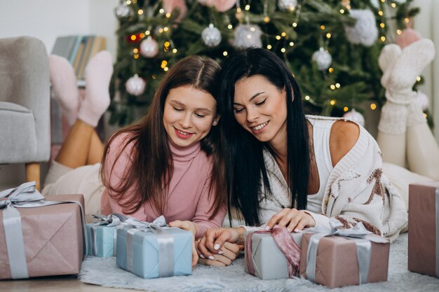 Madre con hija adulta con regalos de navidad por árbol de navidad