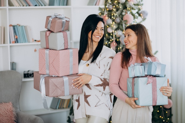 Madre con hija adulta con regalos de navidad por árbol de navidad