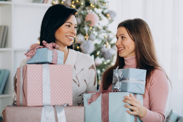 Madre con hija adulta con regalos de navidad por árbol de navidad