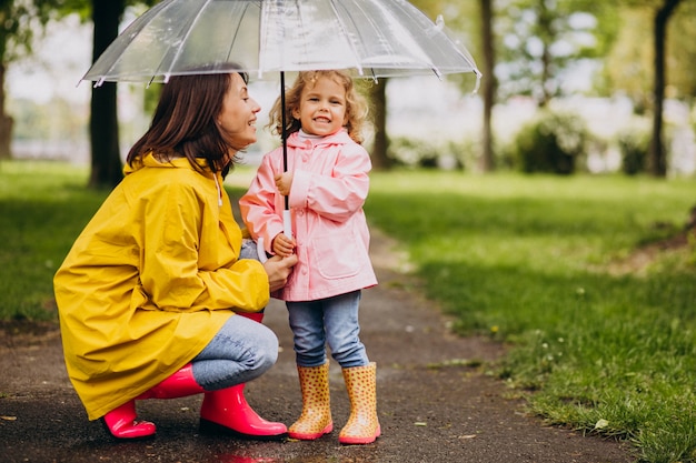 Madre con hija caminando bajo la lluvia bajo el paraguas