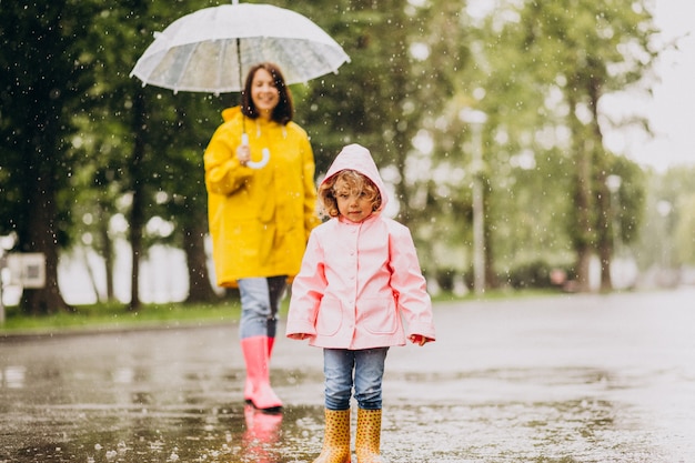 Madre con hija caminando bajo la lluvia bajo el paraguas