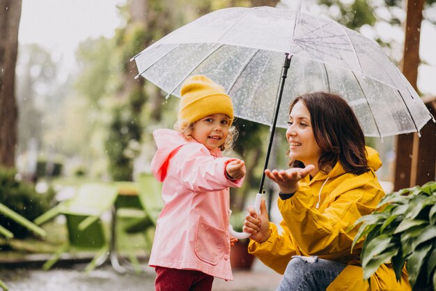 Madre con hija caminando en el parque bajo la lluvia con botas de goma