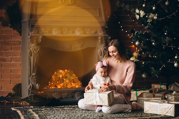 Madre con hija desempaquetando regalos de navidad por arbol de navidad