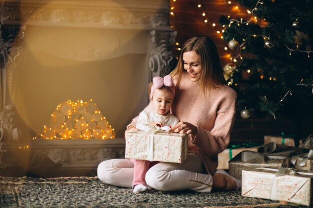 Madre con hija desempaquetando regalos de navidad por arbol de navidad