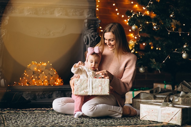 Madre con hija desempaquetando regalos de navidad por arbol de navidad