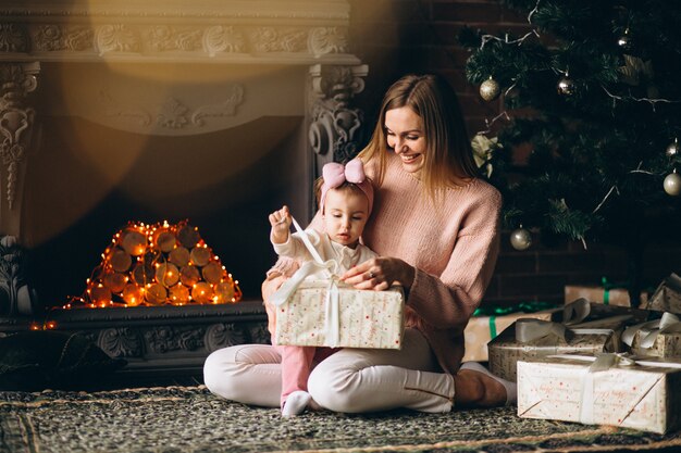 Madre con hija desempaquetando regalos de navidad por arbol de navidad