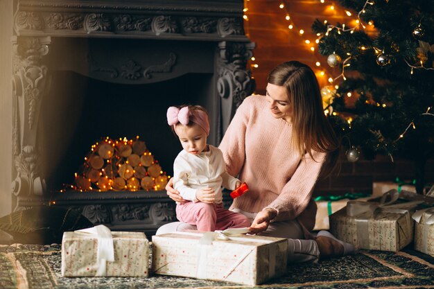 Madre con hija desempaquetando regalos de navidad por arbol de navidad