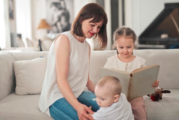 madre, hija e hijo en el sofá miran un libro de imágenes