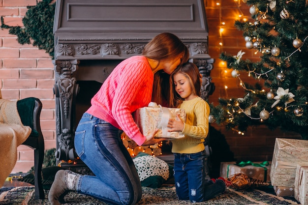 Madre con hija empacando presente por chimenea en navidad