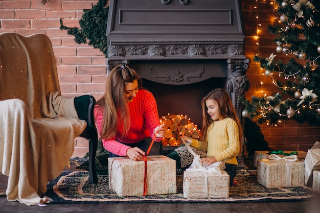 Madre con hija empacando presente por chimenea en navidad