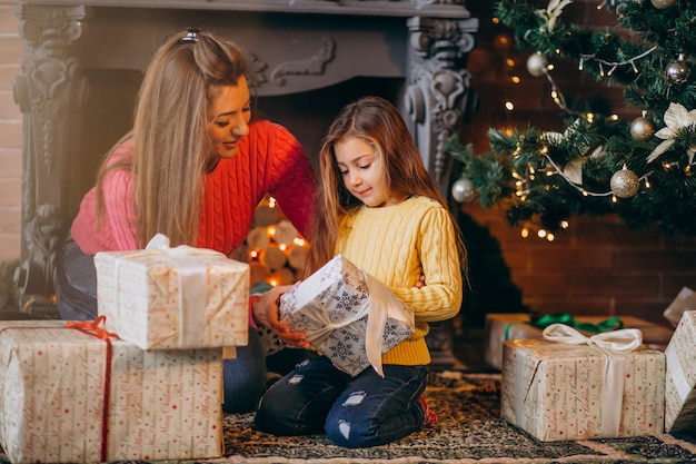 Madre con hija empacando presente por chimenea en navidad