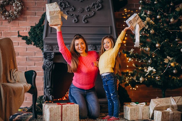 Madre con hija empacando presente por chimenea en navidad