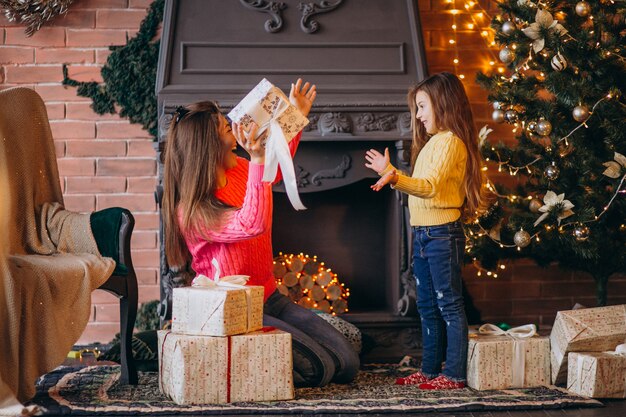 Madre con hija empacando presente por chimenea en navidad