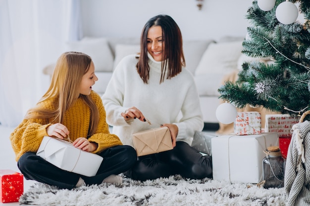 Madre con hija empacando regalos bajo el árbol de navidad