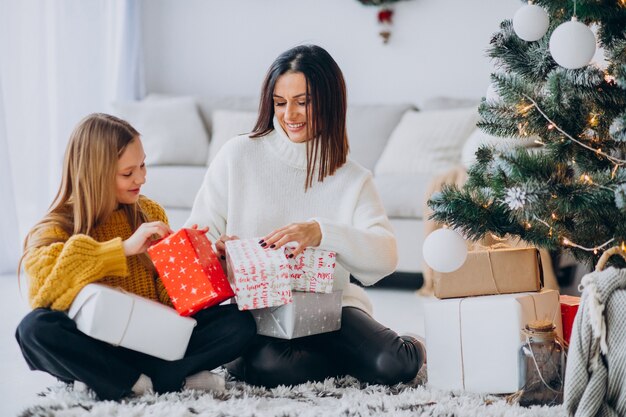 Madre con hija empacando regalos bajo el árbol de navidad