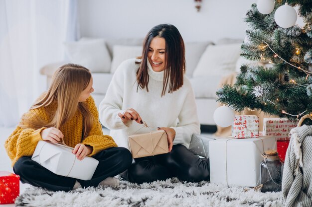 Madre con hija empacando regalos bajo el árbol de navidad