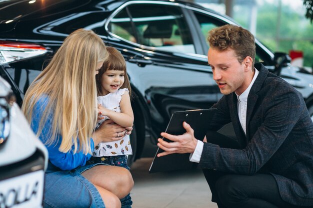 Madre con hija hablando con vendedor en una sala de exposición de automóviles
