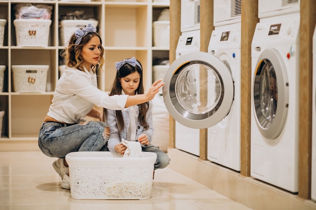 Madre con hija lavando ropa en la lavandería de autoservicio