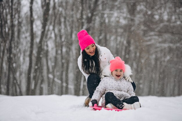 Madre con hija montando en un plato en el parque de invierno