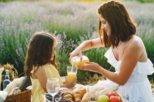 Madre con hija pequeña en campo de lavanda. Mujer hermosa y lindo bebé jugando en el campo del prado. Familia en un picnic.