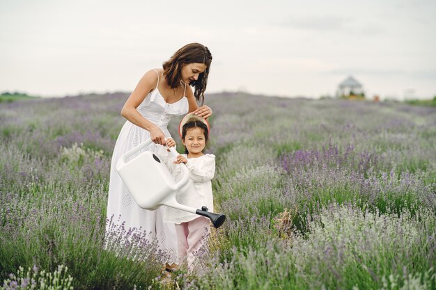 Madre con hija pequeña en campo de lavanda. Mujer hermosa y lindo bebé jugando en el campo del prado. Vacaciones familiares en verano.