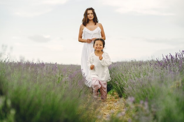 Madre con hija pequeña en campo de lavanda. Mujer hermosa y lindo bebé jugando en el campo del prado. Vacaciones familiares en verano.