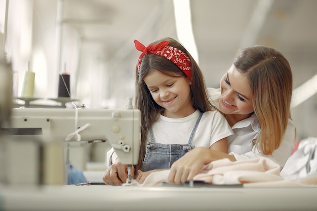 Madre con hija pequeña coser ropa en la fábrica